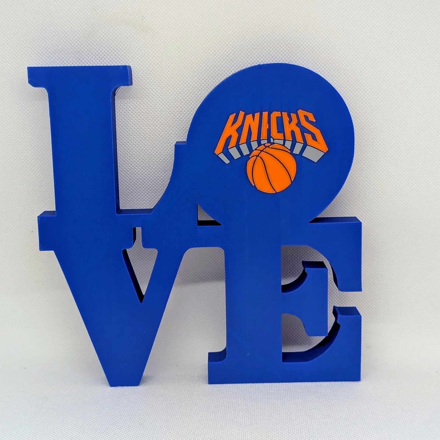 Blue 'LOVE' sculpture with New York Knicks logo and basketball on a white background