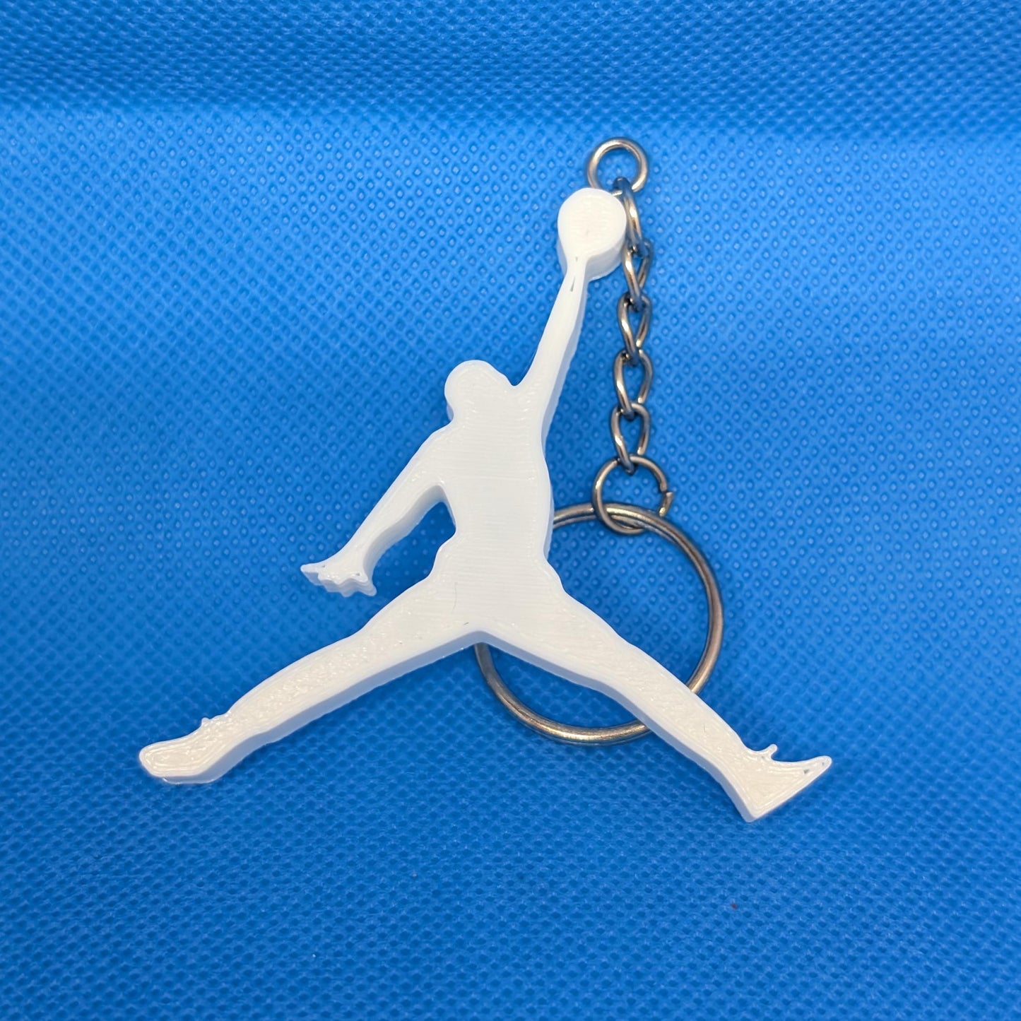 White keychain with a silhouette of a person in mid-air on a blue textured background