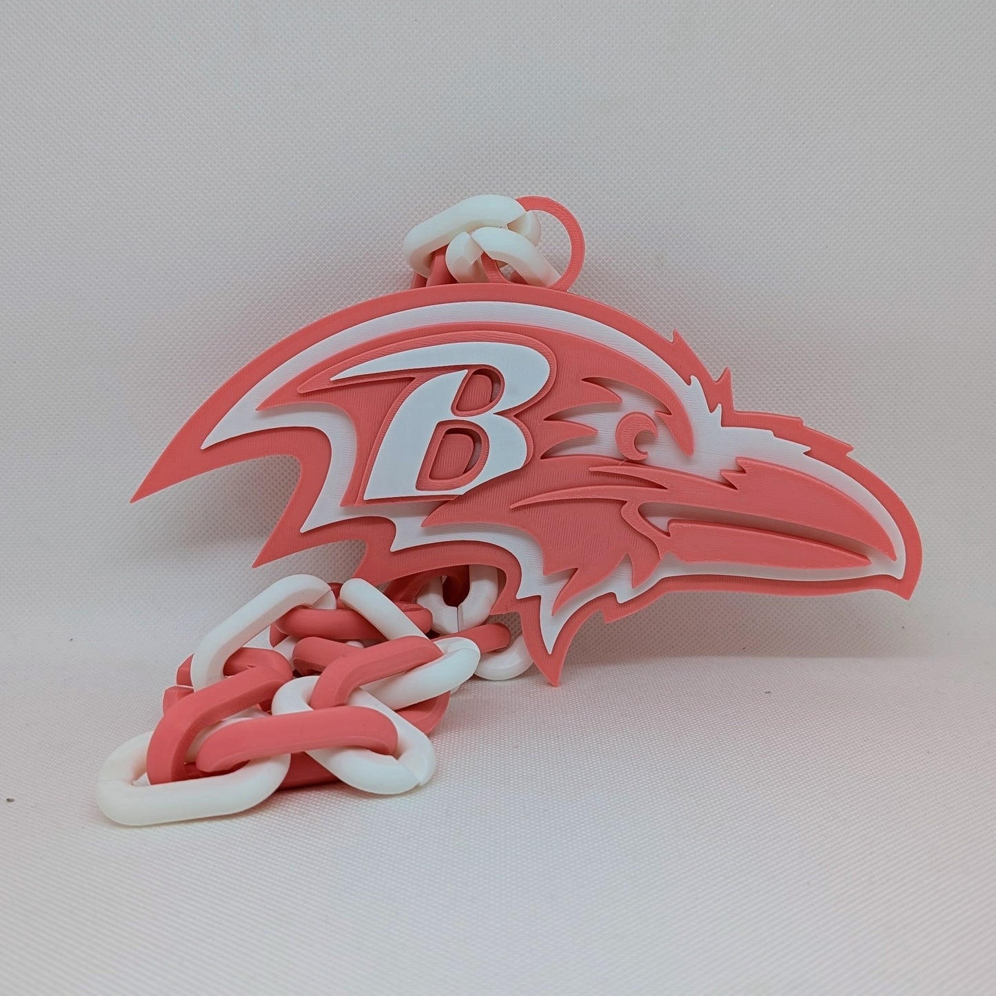 Pink and white Ravens logo with a stylized 'B' on a light pink background