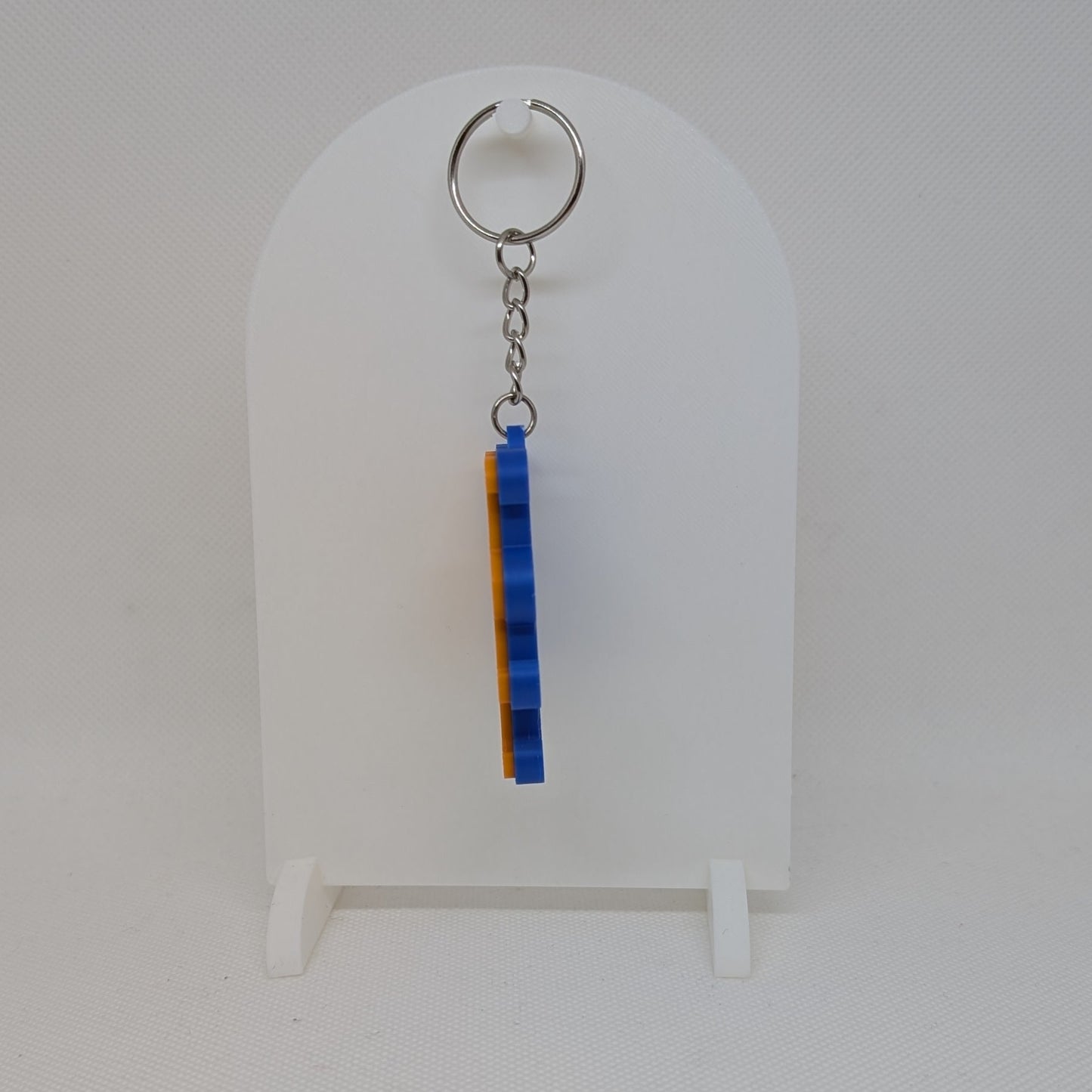 Keychain with blue and silver design on a white stand against a light gray background