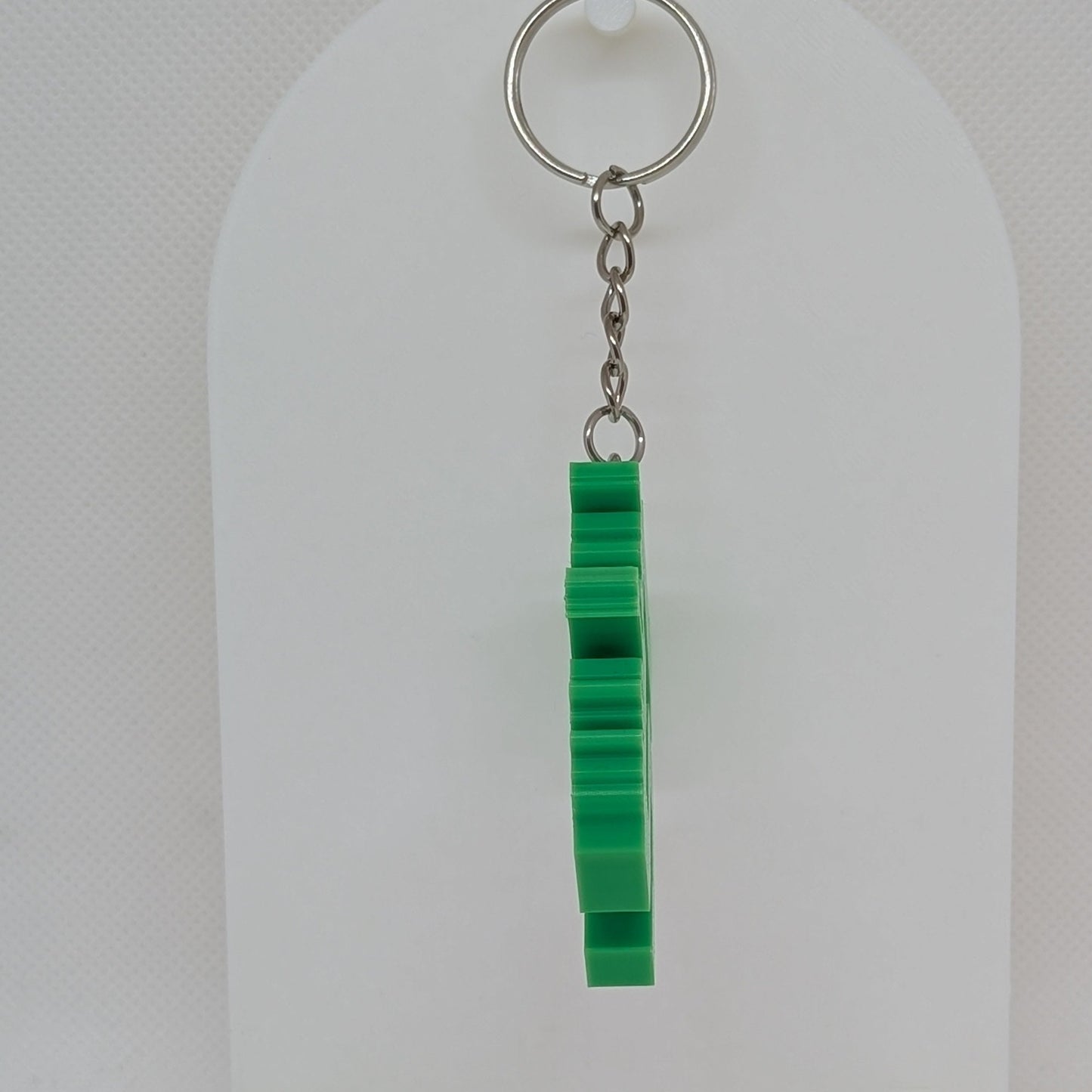 Green keychain on a white stand against a light gray background