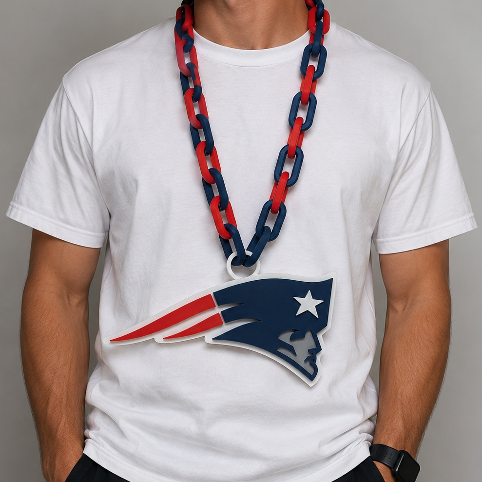 A man wearing a white t-shirt with a large Patriots logo, a red and navy chain necklace, and a navy cap, photographed against a neutral gray background.