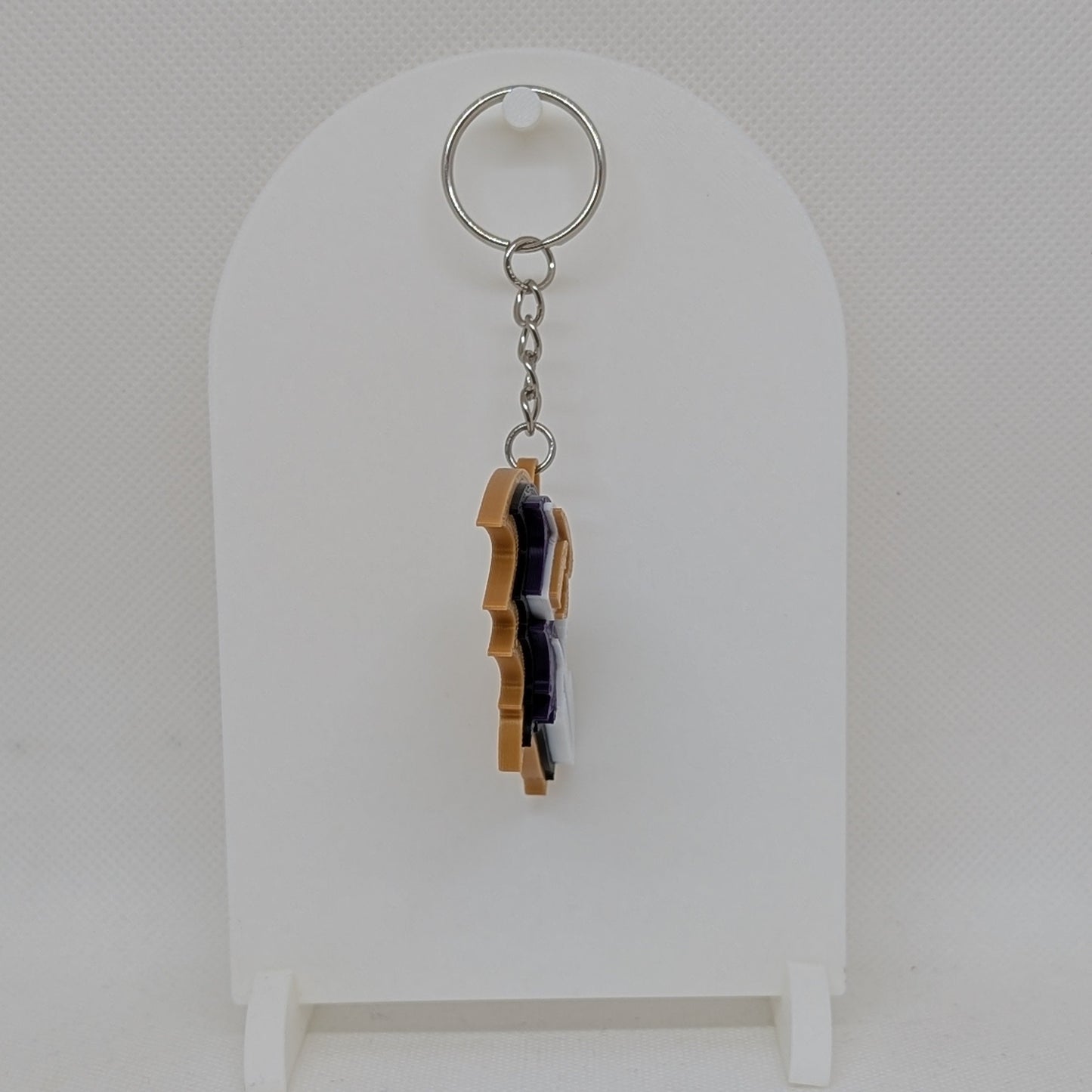 Keychain with a small figurine on a white stand against a light gray background