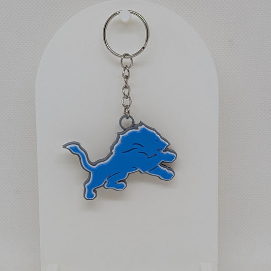 Lions Keychain with blue and silver logo on a white stand against a light gray background