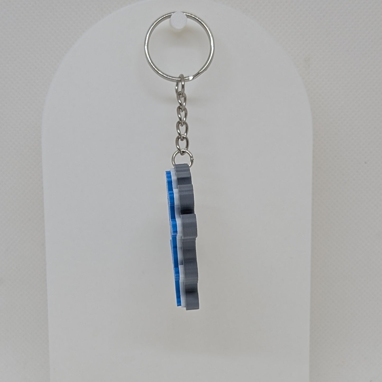 Keychain with striped design on a white stand against a light gray background