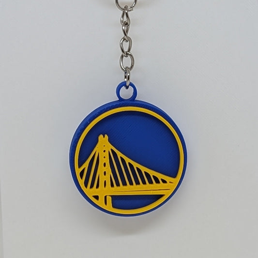 Warriors Keychain with a blue and yellow logo on a white stand